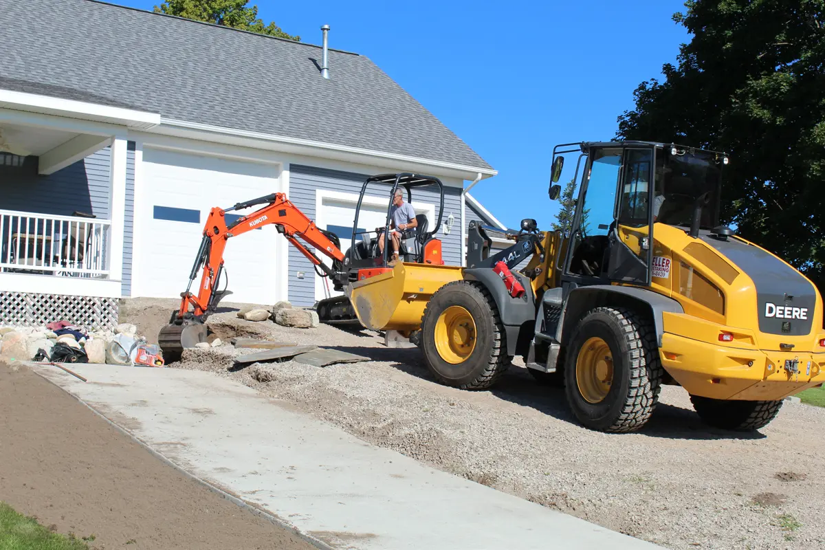 Excavator and loader installing driveway with stone retaining wall