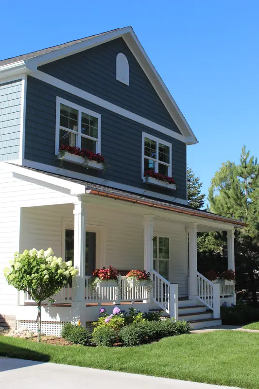 Two-story blue house with white porch and red flower boxes
